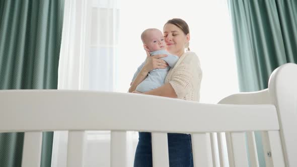 Happy Smiling Mother Hugging and Kissing Her Little Baby Son at Morning Standing in Bedroom with Big