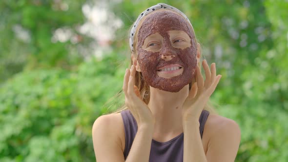 Young Woman with a Face Mask Made From Algae Stands on a Balcony with Green Trees at a Background