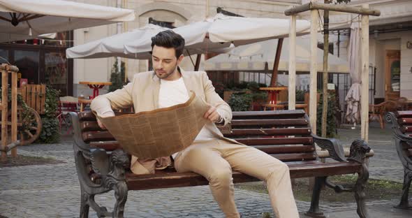 Young Man Sitting On A Bench And Reading An Interesting Article