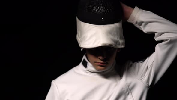 Portrait of Young Guy Fencer Looking Into the Camera and Putting on Sports Protective Mask Helmet