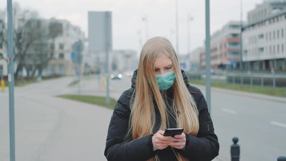 Coronavirus Pandemic: Blonde Woman in a Medical Mask Writing Message on Smartphone