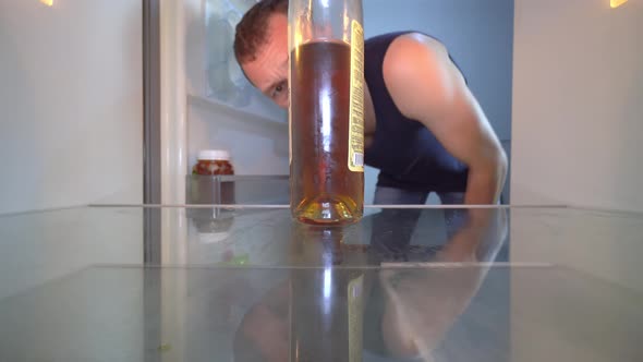 man looks into an empty refrigerator and takes out bottle of alcohol. Alcoholism