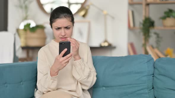 Indian Woman Reacting to Loss on Smartphone on Sofa