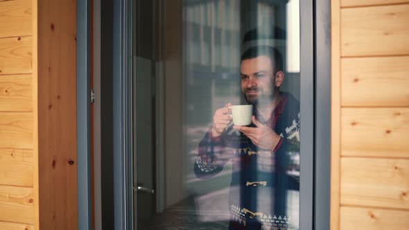 Man Drinking Tea or Coffee Near the Window and Looking Through the Glass