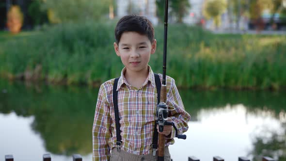 Portrait of the Young Smiled Boy Wearing Special Clothes for Fishing Holding the Fishing Rod