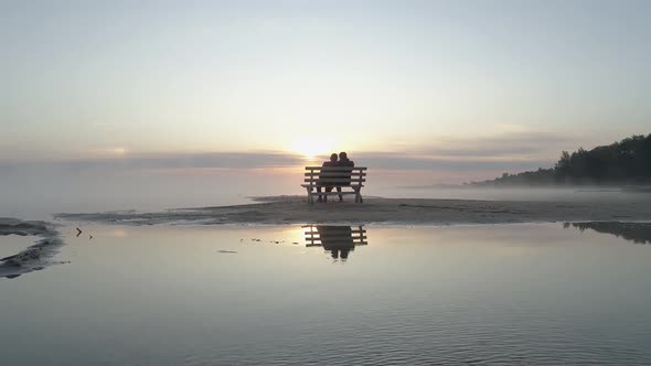 Couple in Love Sitting on a Bench in the Middle of the Lake and Meet the Sunrise