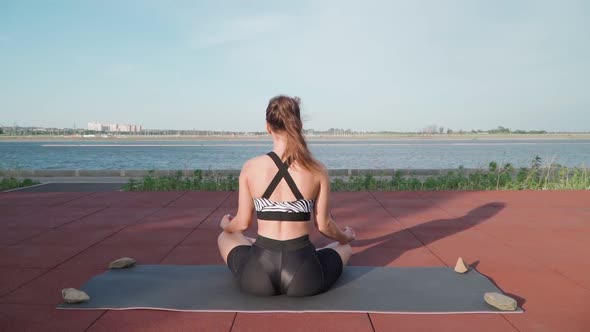 Athletic Woman Sitting in lotus position and Doing Yoga on Lake Background
