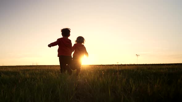Silhouette of Two Little Boys Running Together to the Sun on Open Area Field  Friends Holding Hands