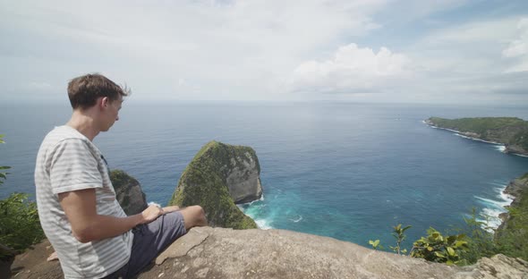 Low Dolly Shot of a Male Tourist Sitting Above the TRex Bay Peninsula with Reveal of the Kelingking