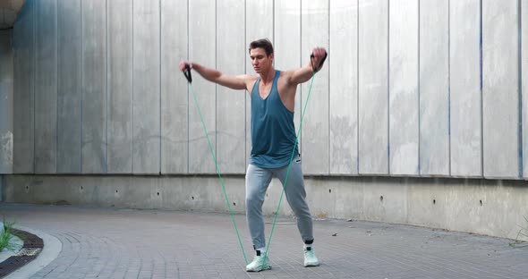 Young Athletic Man Using an Expander to Train His Shoulders Outdoors