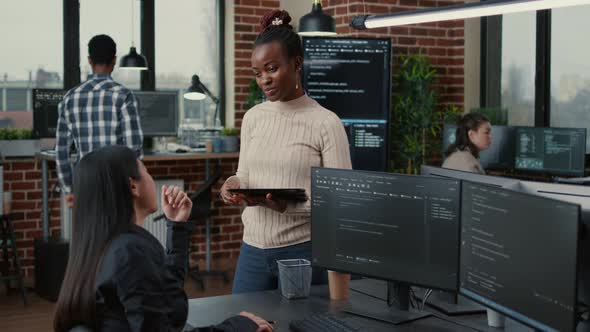 Software Developer Standing Up Holding Digital Tablet Talking with Programer Sitting at Desk