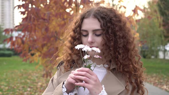 Young Beautiful Woman with a Small Bouquet of Flowers is Walking in the Autumn Park