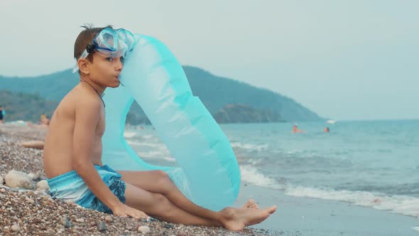 Young Boy Sitting on Sea Beach. Little Boy Preparing Inflatable Circle for Swim