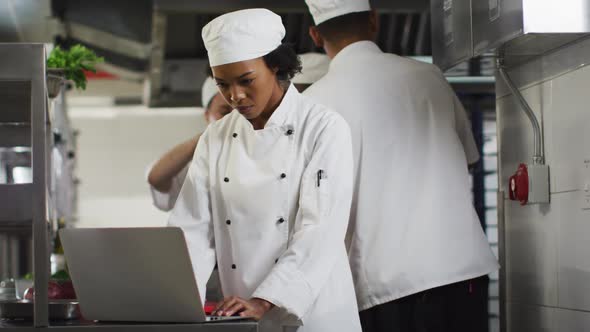 African american female chef using laptop in restaurant kitchen