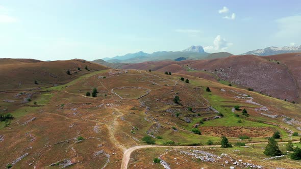 Aerial View of Arid Country Land Some Green Bushes and Trees Blue Sky Mountain in the Horizon Dirty