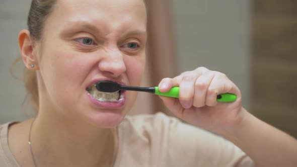 Woman in Beige Tshirt Actively Brushes Her Teeth with Green Toothbrush in the Bathroom at Home