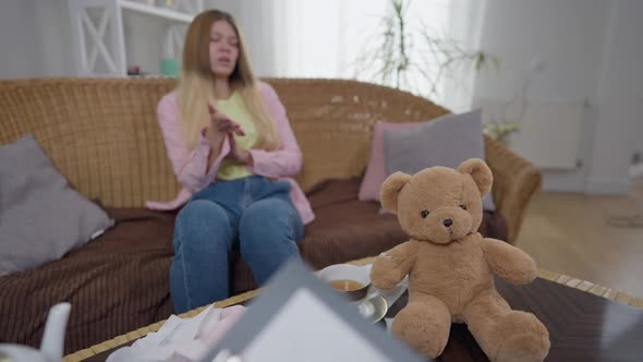 Teddy Bear and Tea Cup on Table with Blurred Young Woman Talking to Unrecognizable Psychologist