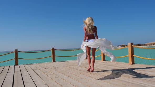 Pretty Young Woman in White Pareo Standing on Pier Near Sea