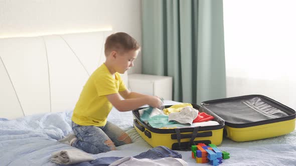 Child Tourist Puts Clothes in a Travel Suitcase for Travel and Recreation. A Little Boy and a