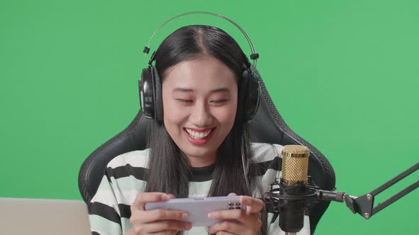 Asian Woman Gamer With Headphone Using Mobile Phone Playing Game On The Green Screen Background