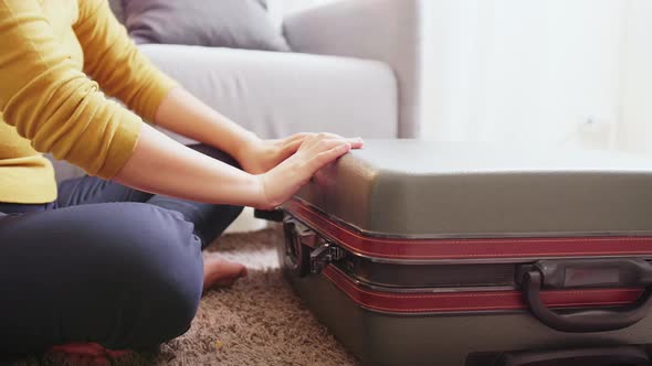 Detail of female hands closing suitcase with clothes. Travel preparation concept.