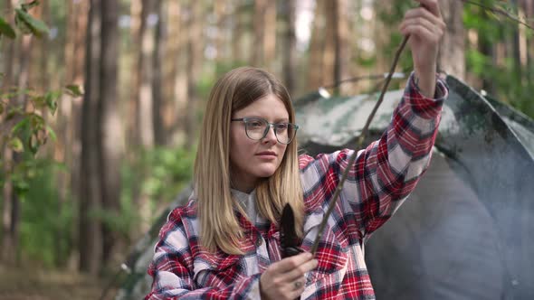 Portrait of Attractive Young Woman Examining Stick Camping in Sunny Forest Outdoors