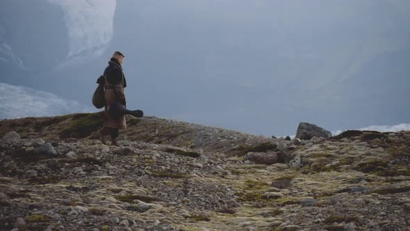 Travelling Man Carrying Guitar And Hiking Over Rocky Landscape