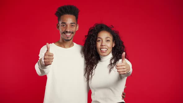 Young African American Couple Making Thumbs Up Sign Over Red Background. Winner