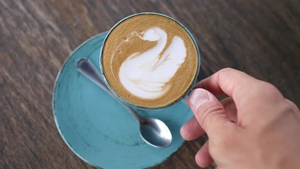 A Hands Picking Up a Mug of Plant Based Coffee Latte From Blue Table