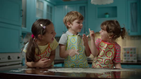 Three kids in aprons playing with dough on kitchen table at home