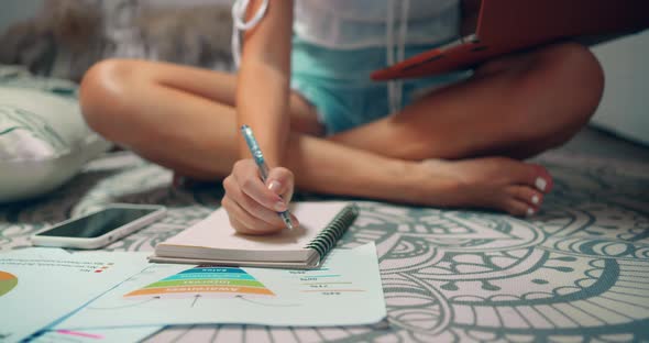 Middle Shot of a Woman Working at Home She Sits on the Cozy Carpet and Writes Notes at Notepad