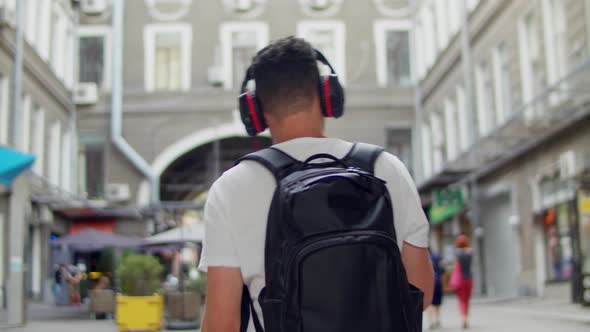 Handsome Young Man Listening Music From His Smartphone in Red Headphones Walk on Street of Town