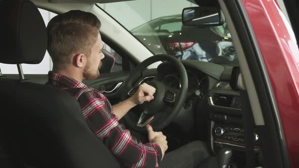 Joyful Handsome Male Customer Showing Thumbs Up Sitting in a New Car at the Dealership