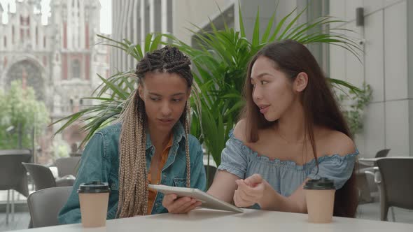 Female Friends Sitting Outside While Chatting and Looking at Tablet