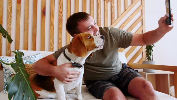 A Joyful Young Man Sitting at Table and Hugging Her Dog Beagle While Making Video Call