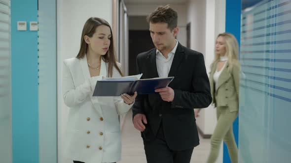 Busy Young Man and Woman Walking in Office Corridor Discussing Project Analyzing Documents As