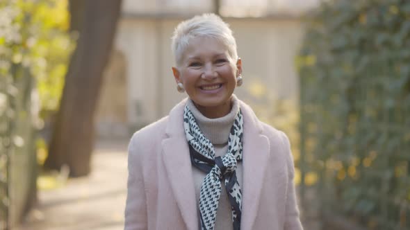 Portrait of Elegant Mature Woman Standing Outdoors and Smiling at Camera