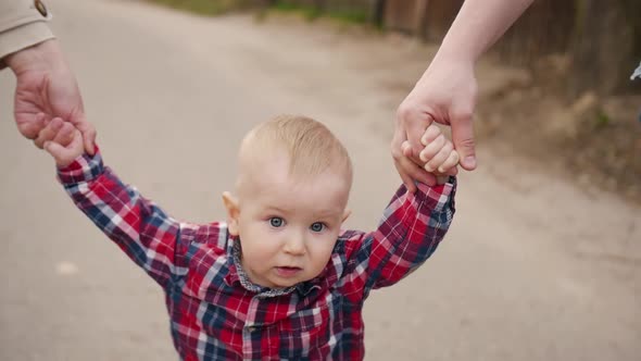 Little Boy Walks Outdoors Holding Parents' Hands