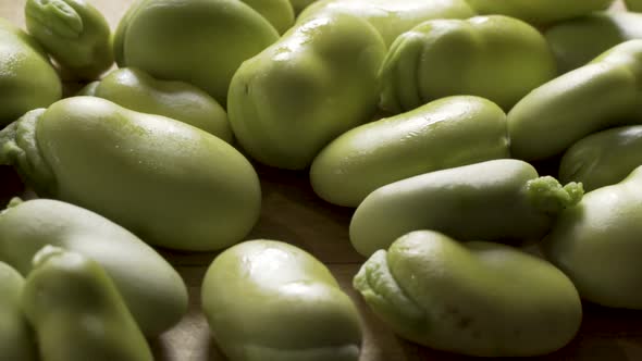 Slider shot from left to right at extreme close up of a pile of sweating, backlit, green fava beans