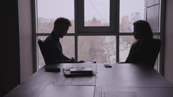 American Businessman and Woman Having Conversation at Table with Phone in Office.