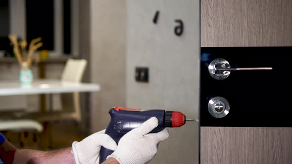 Installing A Lock On The Front Door. A Carpenter In A Special Uniform Repairs The Lock