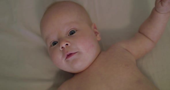 Close Portrait of Blueeyed Perplexed Naked Newborn Baby Moves with Open Arms