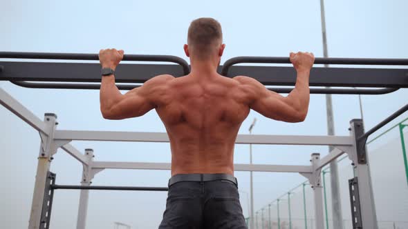 Athletic Man Pumps Up Muscles Doing PullUps Open Sports Ground with Bare Torso