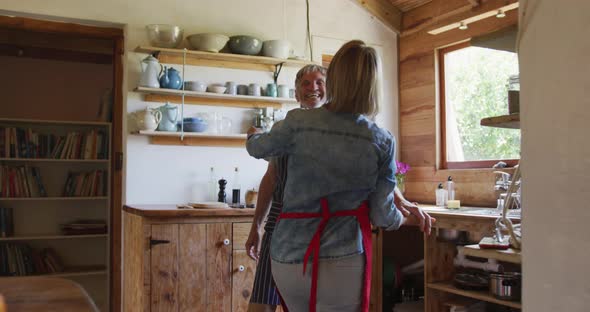 Smiling senior caucasian couple wearing aprons and dancing before cooking in kitchen