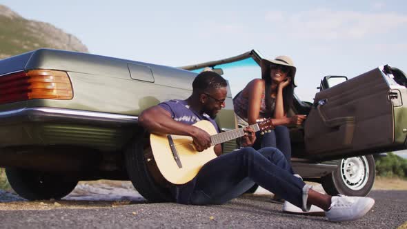African american man playing guitar for his girlfriend while sitting on the road
