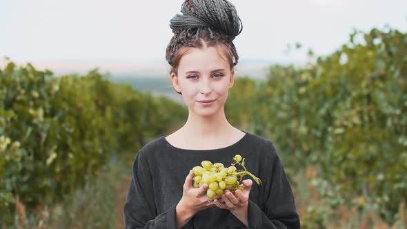 Young Woman with Dreadlocks Holding Grapes in Vineyard