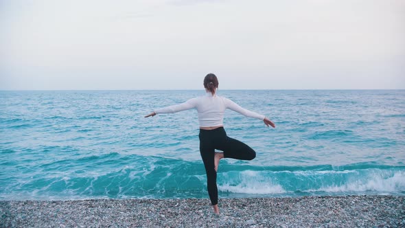 A Gymnastic Woman Balancing on One Leg on the Pebble Beach