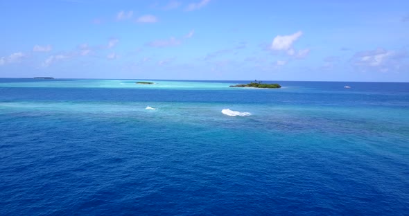 White waves foaming over coral reefs on blue sea around tiny tropical islands of Maldivian archipela