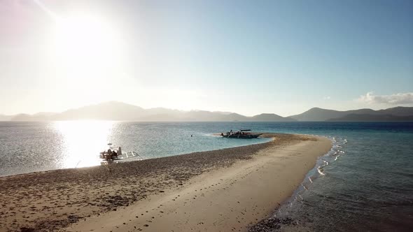 Aerial drone shot of beautiful sunset over the ocean, sandy beach and boats at an island in Palawan,