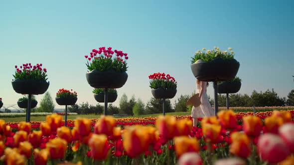 Unknown Woman in Dress Walking Throught Bright Summer Garden in Blooming Flowers